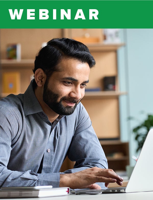 A bearded man smiles while moving the mouse on his laptop. 