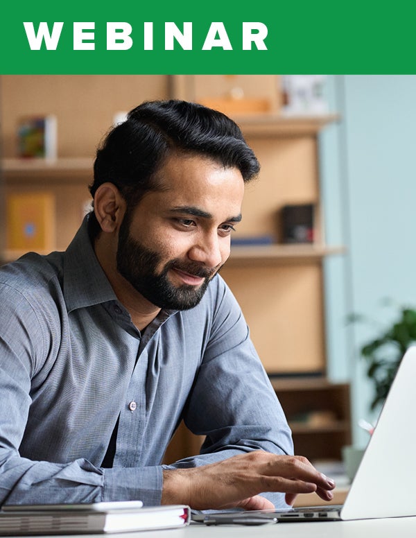 A bearded man smiles while moving the mouse on his laptop.